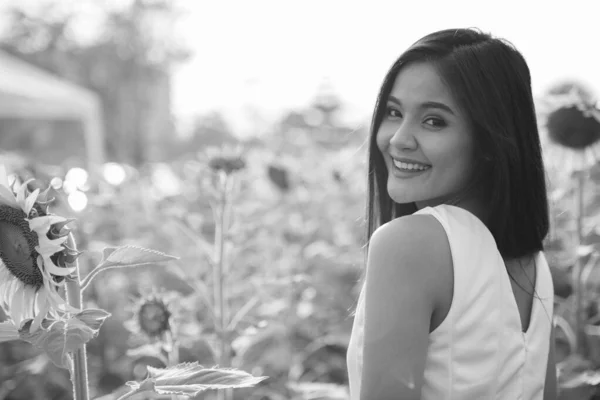 Joven mujer asiática feliz sonriendo y mirando hacia atrás en el campo de los girasoles en flor —  Fotos de Stock