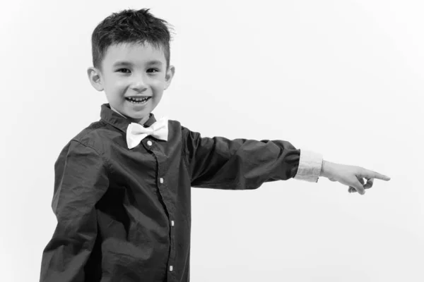 Estúdio tiro de menino feliz bonito sorrindo e apontando o dedo para o lado — Fotografia de Stock
