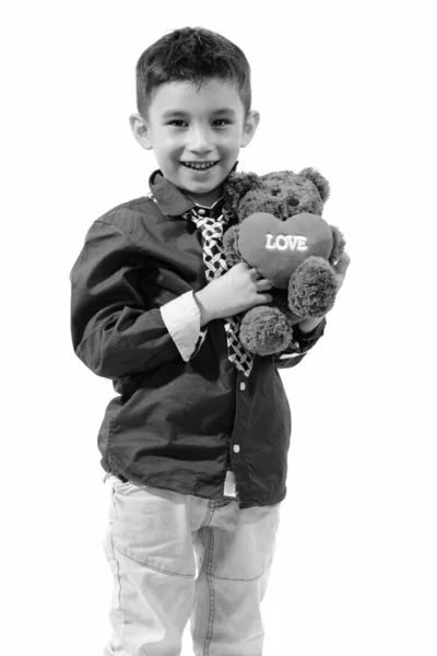 Estudio disparo de lindo niño feliz sonriendo y sosteniendo oso de peluche con corazón y signo de amor —  Fotos de Stock