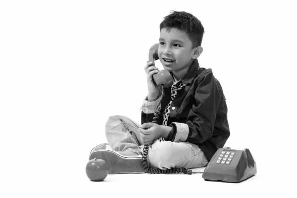 Estúdio tiro de menino feliz bonito sorrindo e falando no telefone velho enquanto pensa — Fotografia de Stock