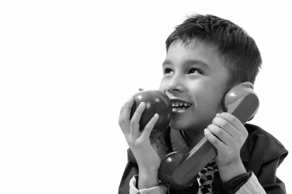Zamyšlený roztomilý šťastný chlapec s úsměvem při rozhovoru na starém telefonu a jíst jablko — Stock fotografie