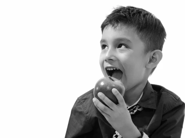 Studio strzał ładny szczęśliwy chłopiec uśmiecha się i jeść jabłko podczas myślenia — Zdjęcie stockowe