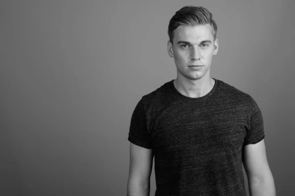 Retrato de homem bonito jovem contra fundo cinza em preto e branco — Fotografia de Stock