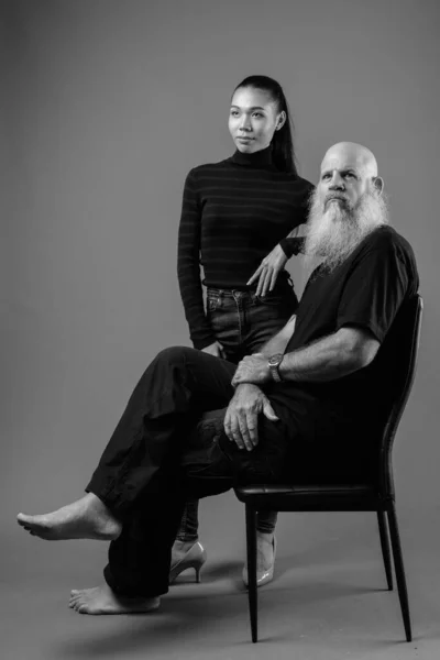 Mature bearded bald man with young Asian transgender woman together in black and white