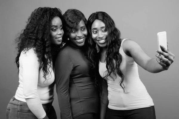 Genç, güzel Afrikalı ikiz kardeşler ve gri arka planda bir arkadaş.