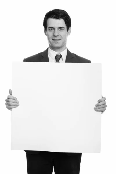 Студійний знімок щасливого бізнесмена, який посміхається і тримає копійку в порожній білій дошці — стокове фото