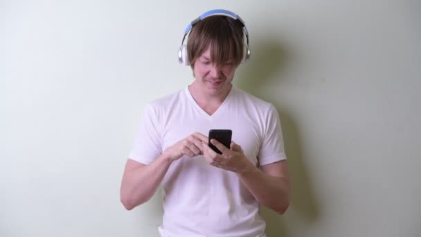 Szczęśliwy młody człowiek z długimi włosami korzystający z telefonu i słuchający muzyki — Wideo stockowe