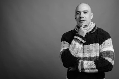 Siyah beyaz arka planda balıkçı yaka kazak giyen yakışıklı, kel adamın stüdyo fotoğrafı.