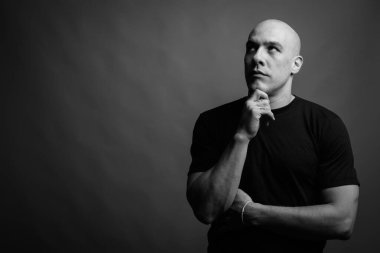 Siyah tişörtlü, siyah ve beyaz arka planlı yakışıklı, kaslı, kel adamın stüdyo fotoğrafı.