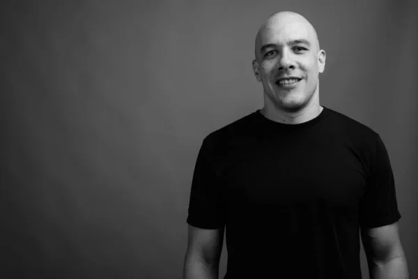 Studio shot of handsome muscular bald man wearing black shirt against gray background in black and white
