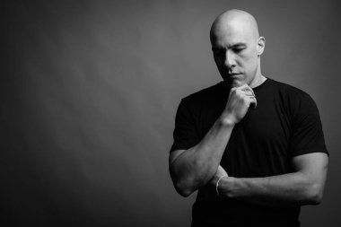 Siyah tişörtlü, siyah ve beyaz arka planlı yakışıklı, kaslı, kel adamın stüdyo fotoğrafı.