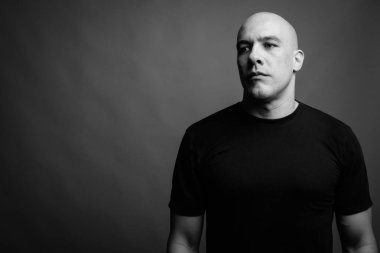 Siyah tişörtlü, siyah ve beyaz arka planlı yakışıklı, kaslı, kel adamın stüdyo fotoğrafı.