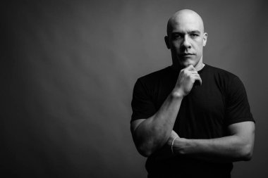 Siyah tişörtlü, siyah ve beyaz arka planlı yakışıklı, kaslı, kel adamın stüdyo fotoğrafı.