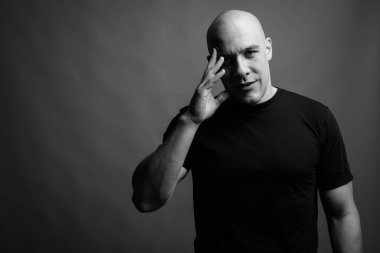 Siyah tişörtlü, siyah ve beyaz arka planlı yakışıklı, kaslı, kel adamın stüdyo fotoğrafı.