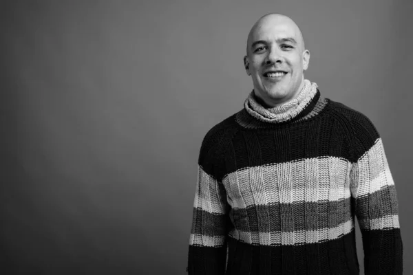 Studio shot of handsome muscular bald man wearing turtleneck sweater against gray background in black and white