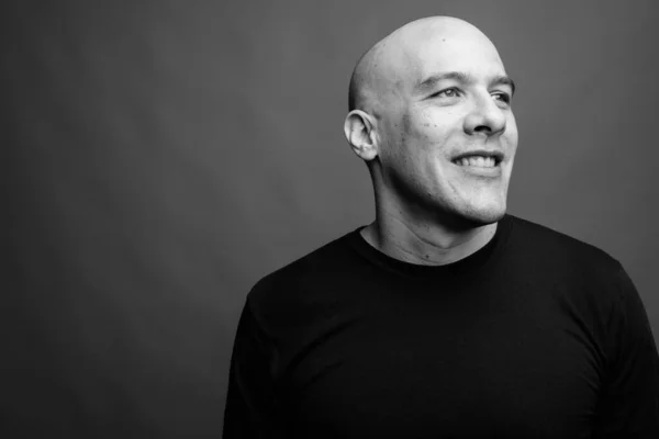 Studio shot of handsome muscular bald man wearing black shirt against gray background in black and white