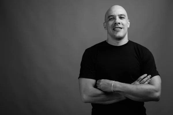 Studio shot of handsome muscular bald man wearing black shirt against gray background in black and white