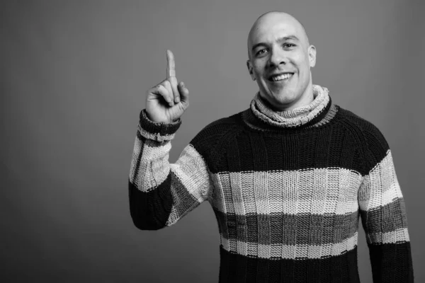 Studio shot of handsome muscular bald man wearing turtleneck sweater against gray background in black and white