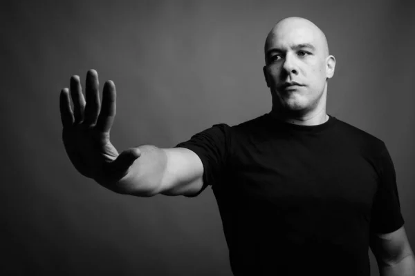 Studio shot of handsome muscular bald man wearing black shirt against gray background in black and white