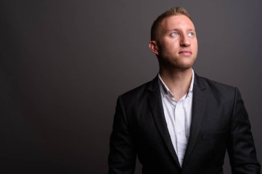 Stüdyo fotoğrafı, sarı saçlı, gri arka planda takım elbiseli bir iş adamı.