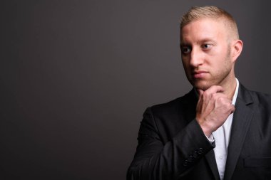 Stüdyo fotoğrafı, sarı saçlı, gri arka planda takım elbiseli bir iş adamı.