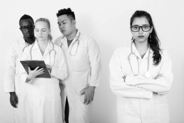 Farklı takımlar olarak çok ırklı doktorların, beyaz arka planda siyah ve beyazlara karşı birlikte çalıştığı bir stüdyo çekimi.