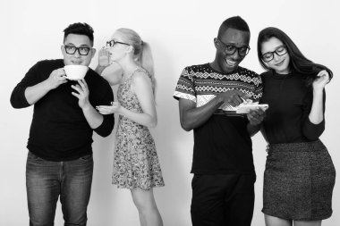 Çok ırklı arkadaşlardan oluşan mutlu bir grup cep telefonu kullanıyor ve arkada arkadaşlarıyla fısıldıyor.