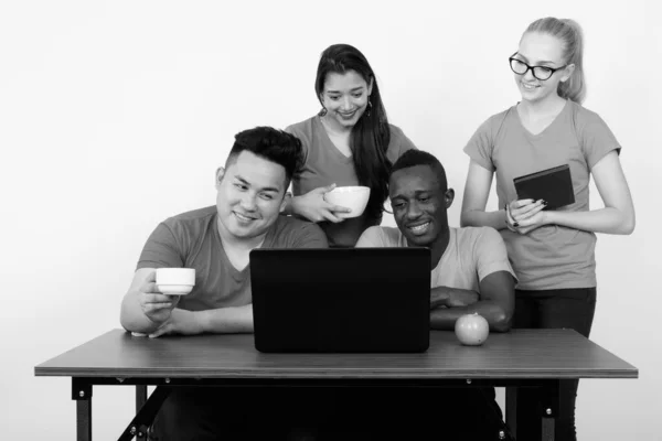 Studio shot of happy diverse group of multi ethnic friends souriant et utilisant un ordinateur portable tout en prenant un café avec pomme verte sur une table en bois ensemble — Photo