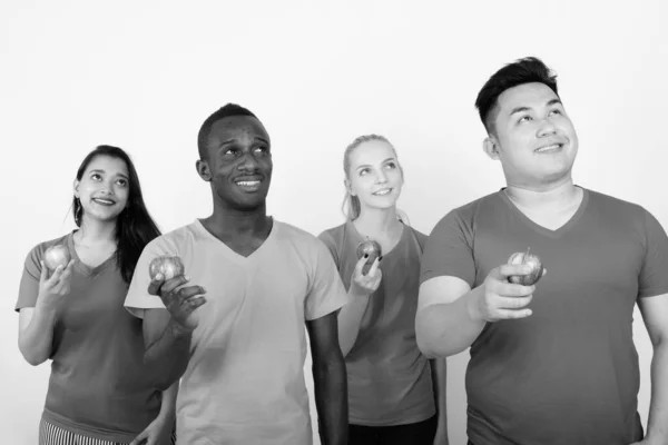 Studioaufnahme einer fröhlichen Gruppe multiethnischer Freunde, die lächeln, während sie denken und einen roten Apfel zusammenhalten — Stockfoto