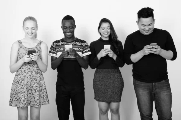 Captura de estudio de feliz grupo diverso de amigos multiétnicos sonriendo mientras usan teléfonos móviles juntos —  Fotos de Stock