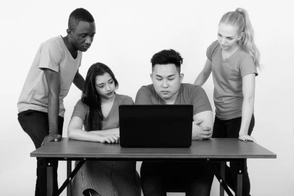 Photo studio de divers groupes d'amis multi-ethniques utilisant un ordinateur portable sur une table en bois ensemble — Photo
