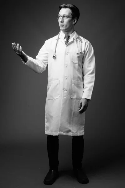 Young handsome man doctor against gray background in black and white — Stock Photo, Image