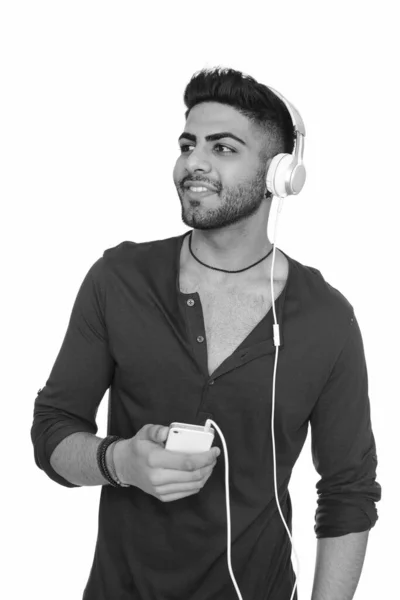 Estúdio tiro de jovem indiano feliz ouvindo música enquanto segurando telefone celular isolado contra fundo branco — Fotografia de Stock