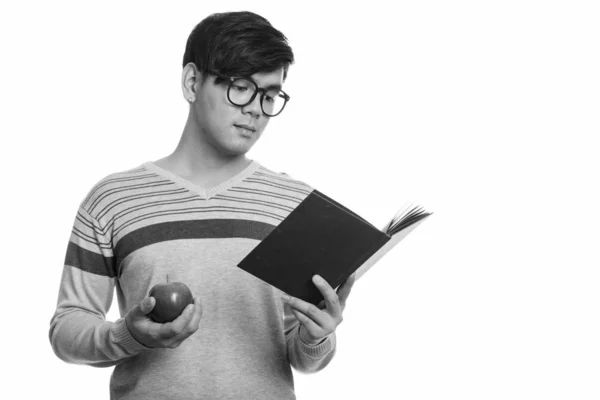 Studio strzał młody przystojny Azjata człowiek czytania książki trzymając czerwone jabłko — Zdjęcie stockowe