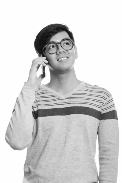 Thoughtful young happy Asian man smiling while talking on mobile phone — Stok fotoğraf