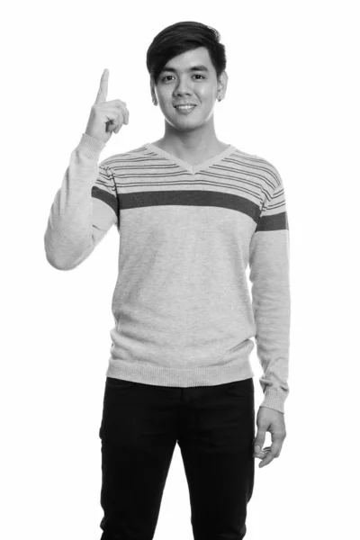 Studioaufnahme eines jungen glücklichen asiatischen Mannes, der lächelt und mit dem Finger nach oben zeigt — Stockfoto