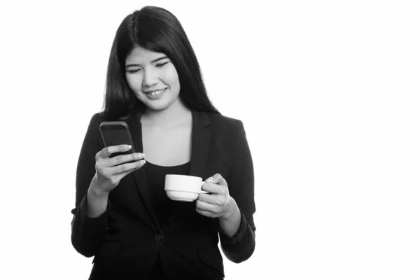 Mladý šťastný asijské podnikatelka s úsměvem při používání mobilních telefonů a hospodářství coffee cup — Stock fotografie