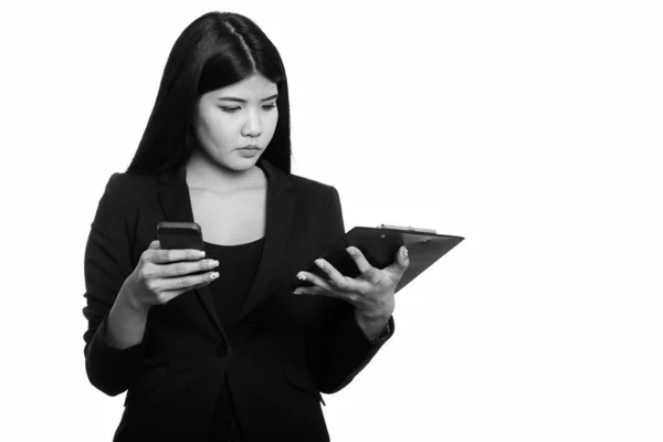 Photo de Studio de jeune femme asiatique sur presse-papiers de lecture tout en tenant le téléphone mobile — Photo