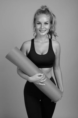 Stüdyoda, sarı saçlı, gri arka planda siyah beyaz spor salonuna hazır güzel bir kadın var.