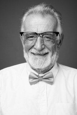 Stüdyo resmi, siyah beyaz arka planda şık kıyafetler giyen yakışıklı, sakallı yaşlı bir adam.