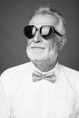 Stüdyo resmi, siyah beyaz arka planda şık kıyafetler giyen yakışıklı, sakallı yaşlı bir adam.