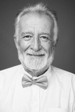 Stüdyo resmi, siyah beyaz arka planda şık kıyafetler giyen yakışıklı, sakallı yaşlı bir adam.