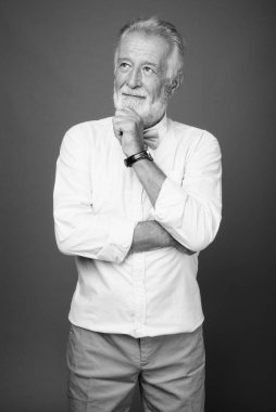 Stüdyo resmi, siyah beyaz arka planda şık kıyafetler giyen yakışıklı, sakallı yaşlı bir adam.