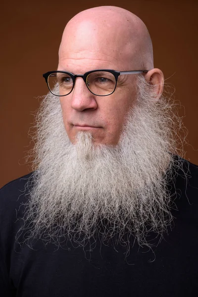 Homem careca maduro com longa barba cinza contra fundo marrom — Fotografia de Stock