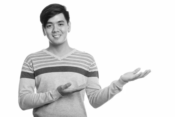 Studio shot of young happy Asian man smiling and showing something — ストック写真