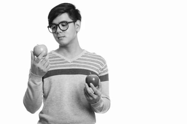 Studio shot of young handsome Asian man holding red apple while looking at green apple — Stock fotografie