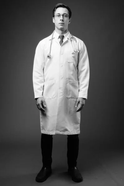 Young handsome man doctor against gray background in black and white — Stock Photo, Image