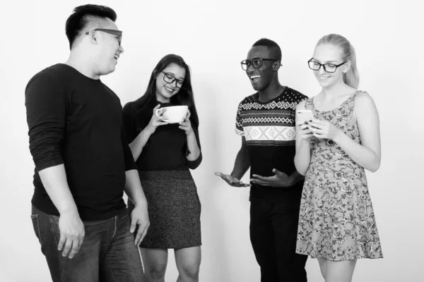 Studio shot van gelukkig diverse groep van multi etnische vrienden samen te glimlachen terwijl het hebben van koffie en het gebruik van mobiele telefoon — Stockfoto