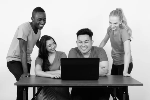 Studio shot of happy diverse group of multi ethnic friends souriant tout en utilisant un ordinateur portable sur une table en bois ensemble — Photo