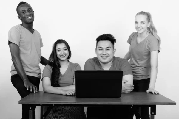 Studio πλάνο της ευτυχισμένη ποικιλόμορφη ομάδα φίλων πολυ εθνοτικών χαμογελώντας ενώ κάθεται μαζί με το laptop στο ξύλινο τραπέζι — Φωτογραφία Αρχείου
